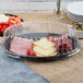 A clear plastic container with olives and a bowl of sauce on a Fineline clear plastic tray.