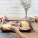 A person holding a Fineline clear plastic tray of food with a clear plastic lid.