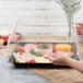 A hand placing a clear plastic lid on a Fineline Platter Pleaser tray of food.