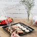 A person's hand holding a clear plastic square dome lid with food on a tray.