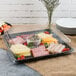 A Fineline black plastic square catering tray with meat, cheese, and vegetables in a plastic container on a table.