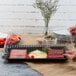 A person using a Fineline clear plastic rectangular dome lid to cover a tray of food on a table.