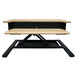 A white oak Luxor two-tier stand up desktop desk on a black base.