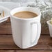 A Hall China bright white mug filled with coffee on a wooden table.