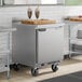 A stainless steel single door worktop freezer on casters with a cutting board and two milkshakes on top.