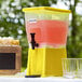 A yellow Choice slim beverage dispenser with a black spigot and glasses.