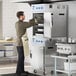 A man in a chef's uniform opening the metal door of a large stainless steel Cooking Performance Group SlowPro cook and hold oven.