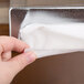 A hand pulling a napkin from a Vollrath stainless steel countertop dispenser.