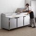 A man in a black apron and gloves using a Beverage-Air pizza prep table to make pizza in a school kitchen.