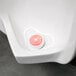 A white plastic urinal screen with a red circular strawberry block in the center.