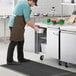 A man in a brown apron putting food into an Avantco undercounter refrigerator in a professional kitchen.