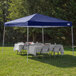 A navy Caravan Canopy tent with a table and chairs set up on grass.