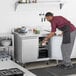 A man in a chef's uniform preparing food on an Avantco worktop refrigerator in a professional kitchen.