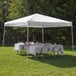 A white Caravan Canopy with tables and chairs set up in the grass.