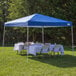 A blue Caravan Canopy tent set up with a white table on grass.