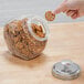 A hand holding a pretzel over a glass jar with a metal lid.