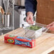 A person using SC Johnson Saran Cling Plus plastic wrap to cover a bowl of greens.