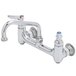 A chrome Equip by T&S wall mounted faucet with two lever handles and a swing spout.