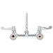 A chrome wall mount faucet with wrist handles and a swing spout.