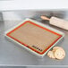 A baking tray with cookies and a Sasa Demarle SILPAT&reg; baking mat on a metal surface.