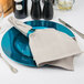 A Tabletop Classics by Walco blue plastic charger plate with silverware and a napkin on it.