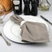 A white Tabletop Classics by Walco plastic charger plate with silverware and a napkin on it.