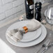 A white plate with a Tabletop Classics copper napkin ring on a napkin on it.
