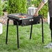 A person using a Backyard Pro double burner outdoor range with a griddle to cook food on a table outdoors.