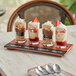An Acopa flight tray with Straight Up Tasting Glasses filled with desserts on a table.