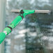 An Unger ErgoTec SwivelLoc squeegee with a green handle cleaning a window.