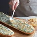 A close-up of a spoon spreading minced garlic on a slice of bread.