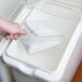 A person using a Rubbermaid clear plastic utility scoop to scoop ice into a glass container.