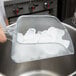 A person using a Rubbermaid clear plastic utility scoop to get ice from a clear glass container.