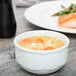 A Tuxton bright white china bouillon cup filled with soup next to a plate of food.