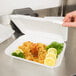 A hand holding a Genpak white styrofoam container of food.