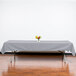 A table with a grey Intedge tablecloth on it with a vase of flowers.