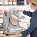 A person in a blue uniform rolling dough into an Estella countertop dough sheeter.