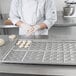 A woman in a white chef's uniform using a Chicago Metallic slider bun pan to prepare dough.