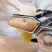 A gloved hand uses a Weston Roma Manual Pasta Machine to make noodles on a kitchen counter.
