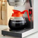 A glass coffee decanter with an orange handle labeled 'WebstaurantStore' placed on a coffee maker.