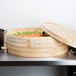 A 24" bamboo steamer set with vegetables in it.