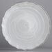 A white scalloped glass charger plate with a silver rim.