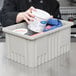 A person holding a gray Metro Tote Box filled with food on a counter.