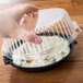 A hand reaching into a clear plastic container with a dome lid.