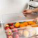 A hand using a Carlisle StorPlus universal flat lid to cover a container of fruit.