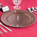 A rose gold beaded charger plate with silverware on a table.