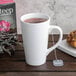 A white Libbey tall bistro mug filled with tea with a tea bag next to it.