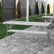 A Regency stainless steel folding table with a white tablecloth on a brick patio.