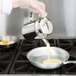 A person using the Vollrath stainless steel batter dispenser to pour liquid batter into a pan.