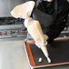 A person in a black and white apron using an Ateco canvas pastry bag to pipe pastries.